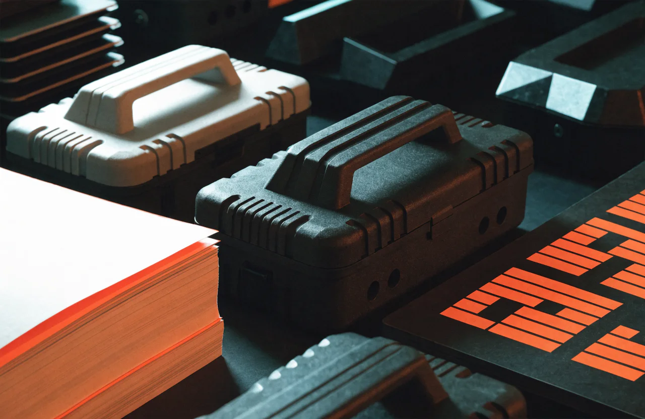 A field logistics table with rugged cases, procurement documents, and an orange routing mark.